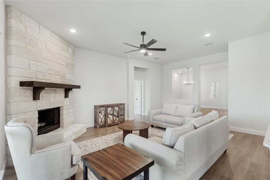 Living room with floor-to-ceiling stone fireplace, light gray sofas, wood coffee tables, and ceiling fan on hardwood floors