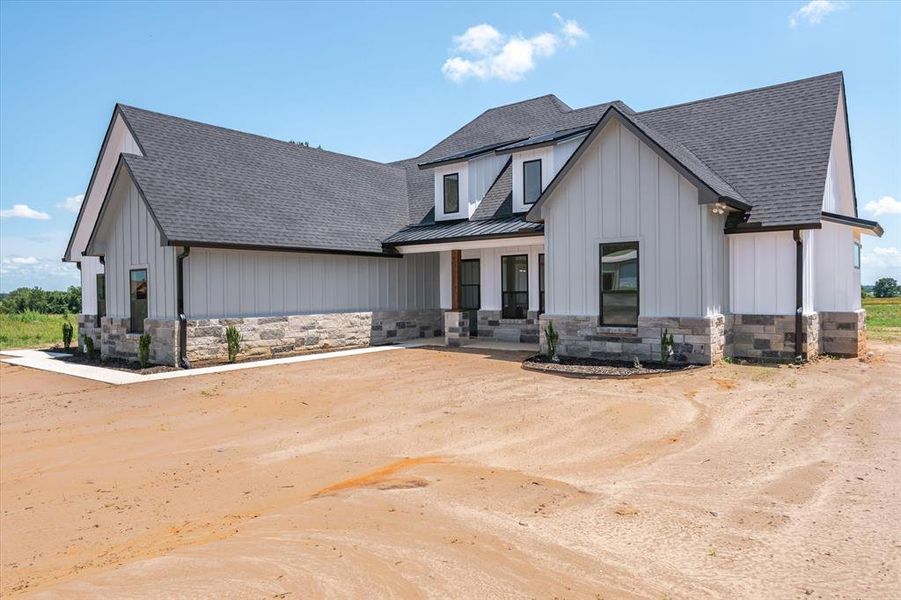 Modern farmhouse featuring stone siding, a shingled roof, board and batten siding, and covered porch