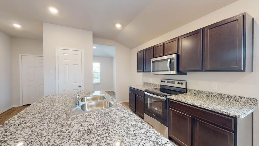 Kitchen featuring dark wood-finish cabinetry, stainless steel appliances, speckled granite countertops, and a double basin sink