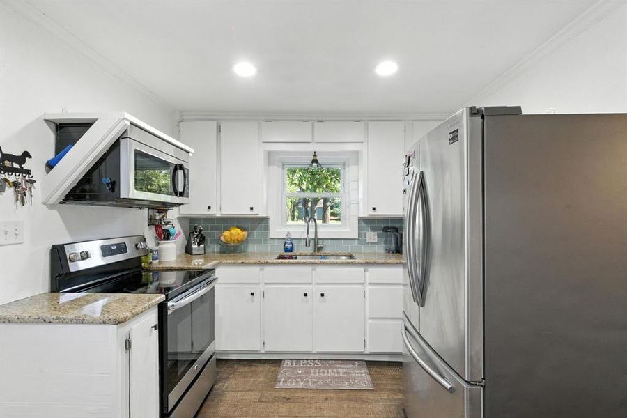 Kitchen with appliances with stainless steel finishes, crown molding, tasteful backsplash, white cabinets, and light stone counters Kitchen with appliances with stainless steel finishes, crown molding, tasteful backsplash, white cabinets, and light stone counters