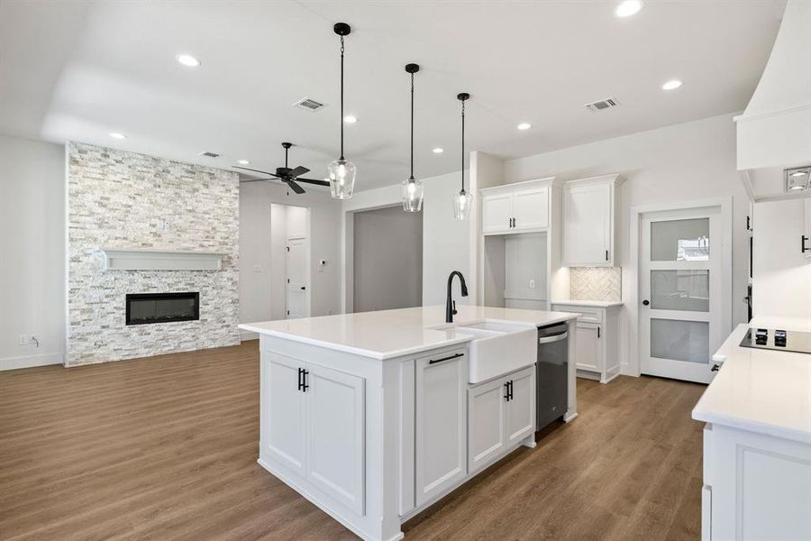 Kitchen featuring pendant lighting, white cabinets, a center island with sink, open floor plan, and light stone countertops