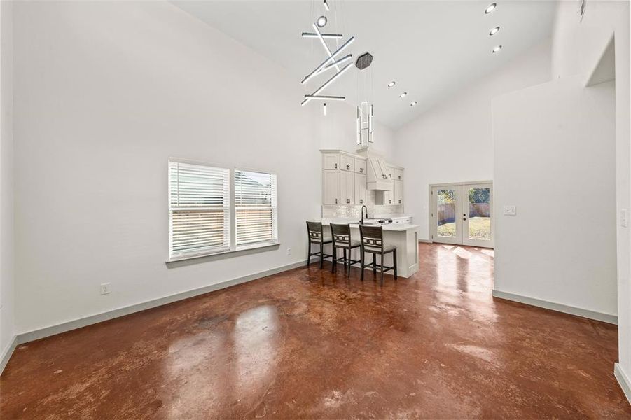 Dining area featuring healthy amount of natural light, concrete floors, french doors, high vaulted ceiling, and recessed lighting