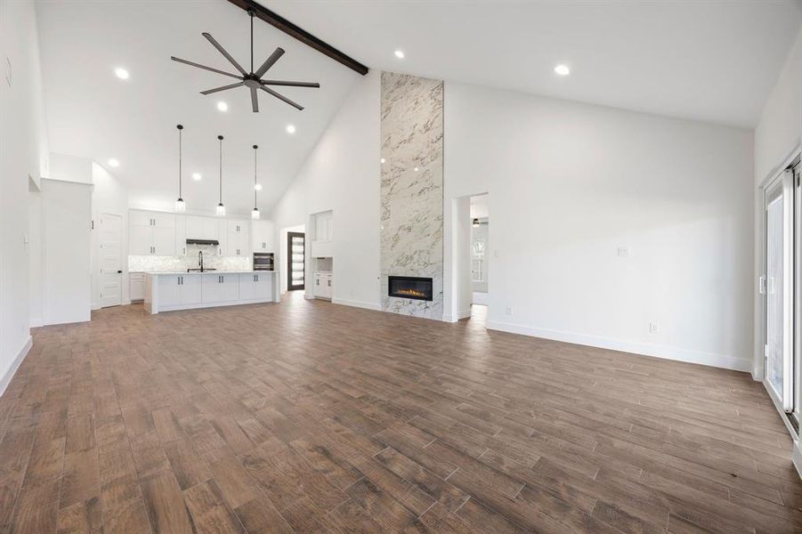Spacious interior featuring a vaulted ceiling with exposed beam, wood-finish flooring, and a contemporary fireplace with a tall stone surround Spacious interior featuring a vaulted ceiling with exposed beam, wood-finish flooring, and a contemporary fireplace with a tall stone surround