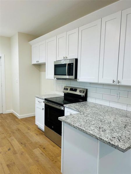 Kitchen featuring white cabinets, appliances with stainless steel finishes, light wood-type flooring, and tasteful backsplash