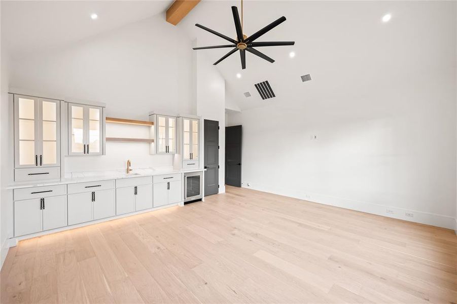 Vaulted ceiling room featuring light wood-finish flooring, a built-in wet bar with a beverage refrigerator, light gray cabinetry, and a contemporary ceiling fan