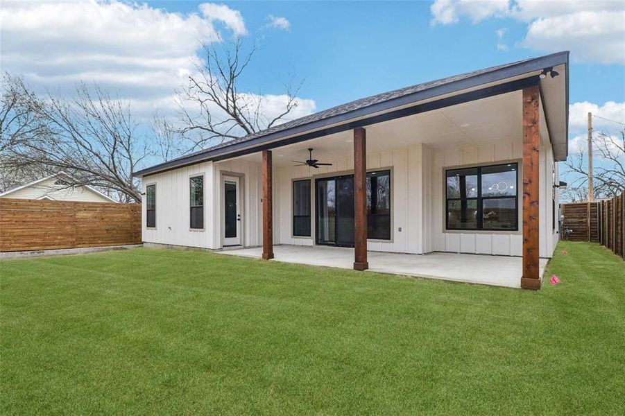 Rear exterior featuring white vertical siding and a covered patio with dark wood support beams