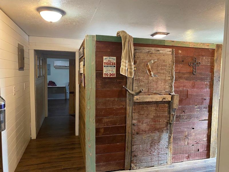 Corridor featuring a textured ceiling, dark wood-style floors, wooden walls, and an AC wall unit