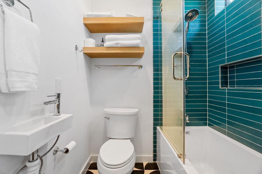Bathroom featuring a wall-mounted rectangular sink with chrome faucet, a white toilet, and wood-finish floating shelves