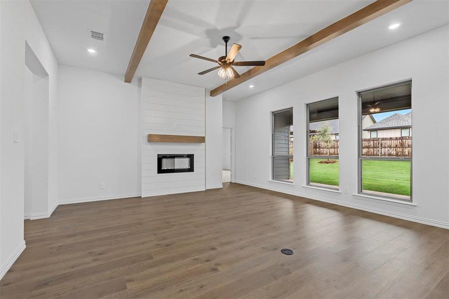 Unfurnished living room with ceiling fan, beamed ceiling, a fireplace, and dark hardwood / wood-style flooring