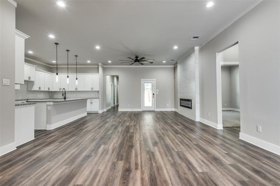 Unfurnished living room with ornamental molding, ceiling fan, recessed lighting, dark wood finished floors, and a tiled fireplace Unfurnished living room with ornamental molding, ceiling fan, recessed lighting, dark wood finished floors, and a tiled fireplace