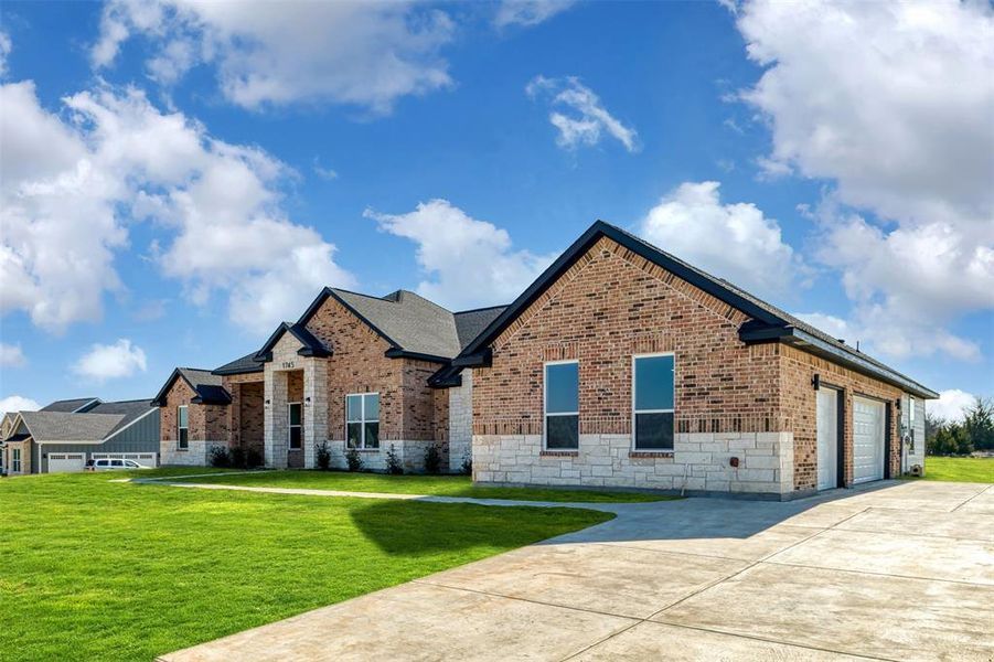View of front of home featuring stone siding, an attached garage, brick siding, a front lawn, and driveway