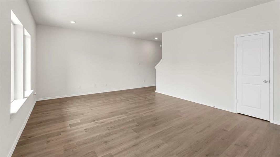 Spacious room featuring light-colored flooring, white walls, recessed lighting, and three tall windows providing natural light
