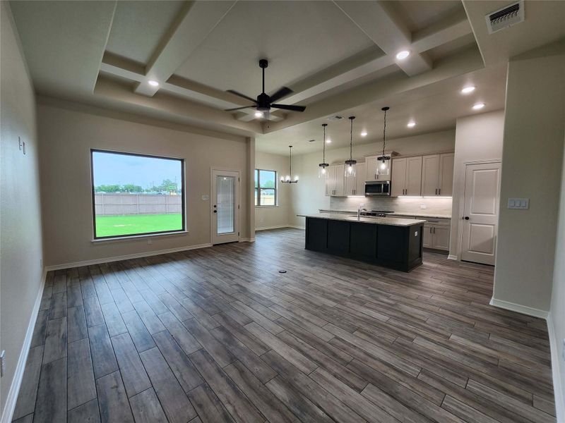 Open-concept living space featuring wood-finish plank flooring and a tray ceiling with recessed lighting and a ceiling fan