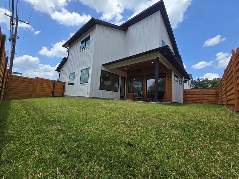 Rear view of the yard with lots of grass space and shaded cover under the porch.