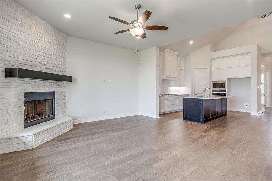 Unfurnished living room with ceiling fan, a fireplace, light hardwood / wood-style floors, and lofted ceiling