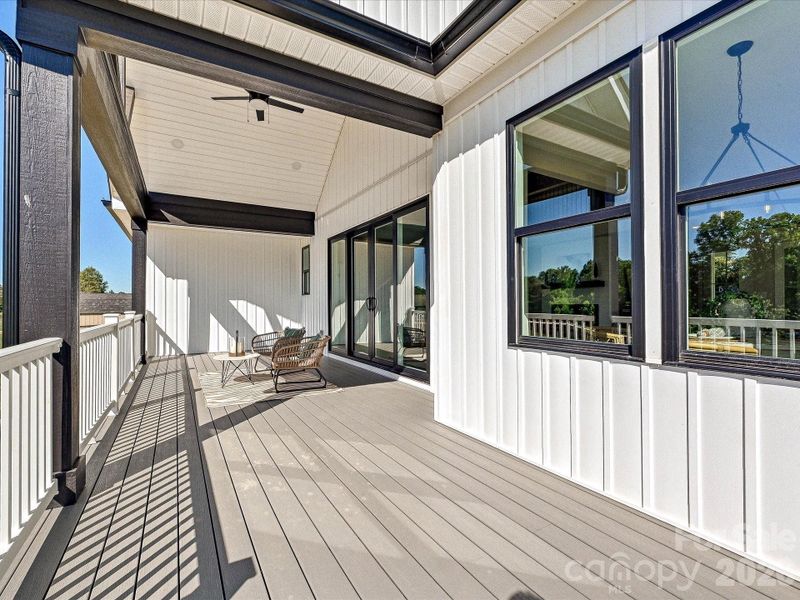 Covered back deck showcases vaulted wood-accented ceilings, composite decking, and seamless indoor-outdoor living with peaceful wooded views.