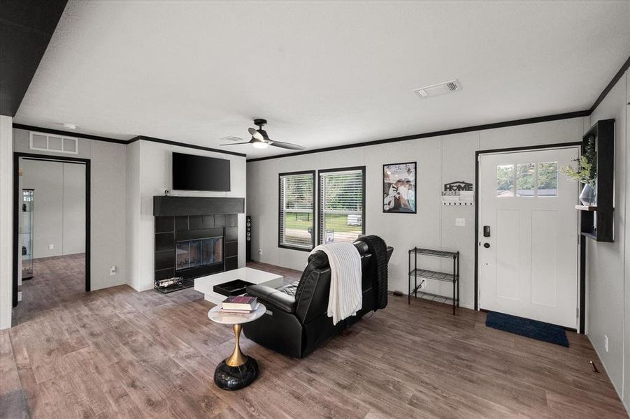 Spacious living area featuring wood-finish flooring, a black tiled fireplace with a mantel, and a multi-pane front door. Spacious living area featuring wood-finish flooring, a black tiled fireplace with a mantel, and a multi-pane front door.