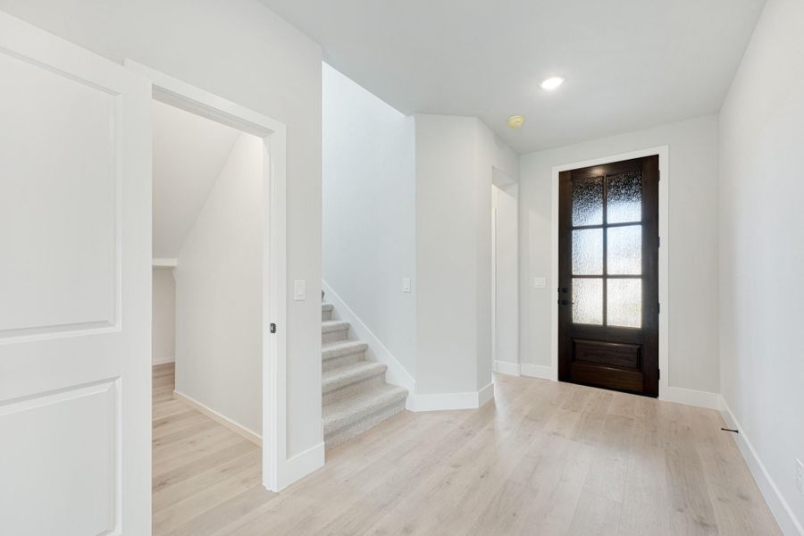 Entryway with dark wood glass-panel front door, light hardwood floors, and staircase with under-stair storage.