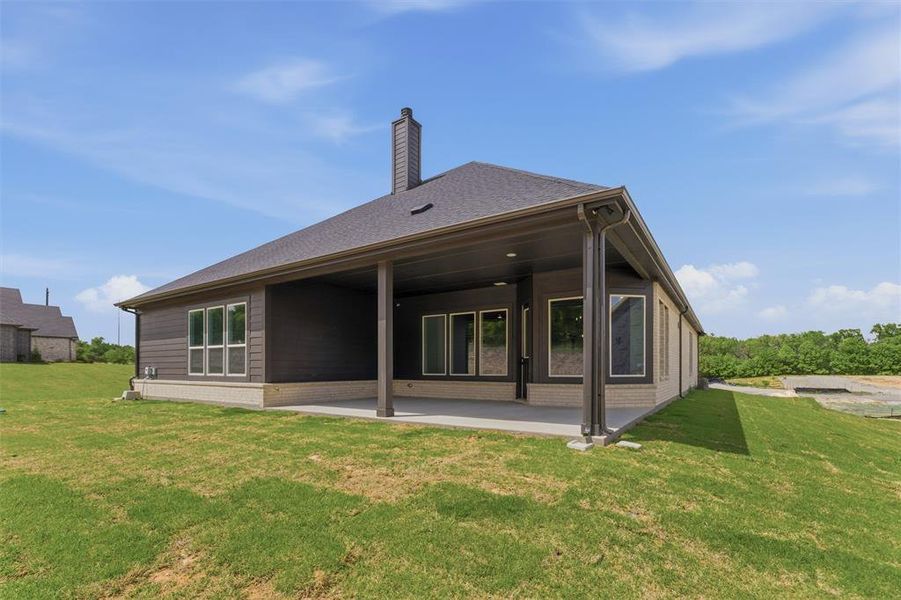 Back of property featuring a patio, a yard, brick siding, a chimney, and a shingled roof