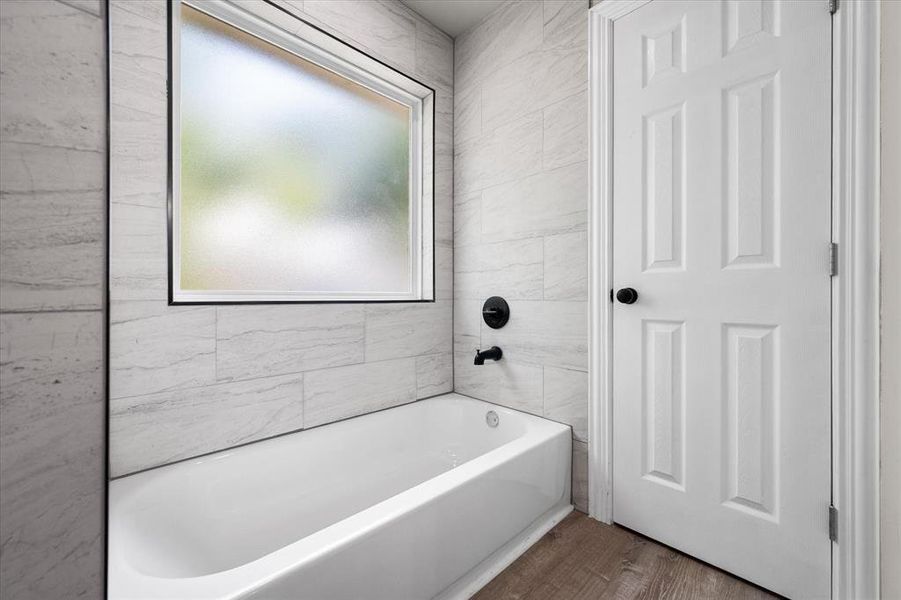 Bathroom featuring a white soaking tub, matte black plumbing fixtures, and a horizontal frosted window