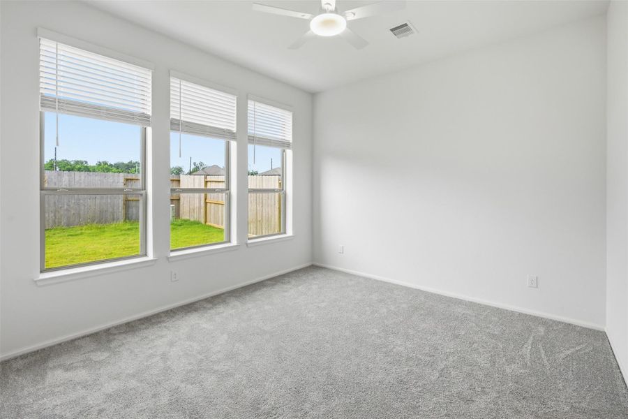 Bright and airy bedroom with large windows, plush carpeting, and a ceiling fan, overlooking a well maintained backyard.
