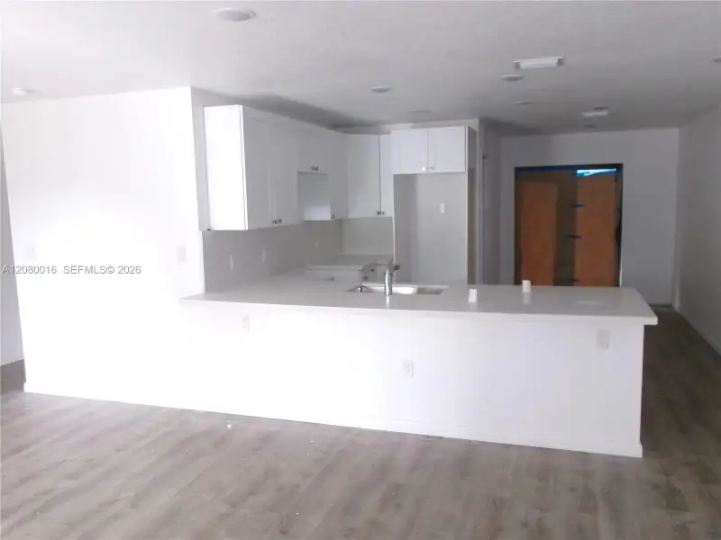 Kitchen featuring white cabinetry, solid-surface countertops, integrated sink, recessed lighting, and wood-finish flooring