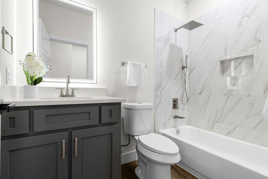 Full bathroom featuring hardwood / wood-style floors, tiled shower / bath combo, toilet, and vanity