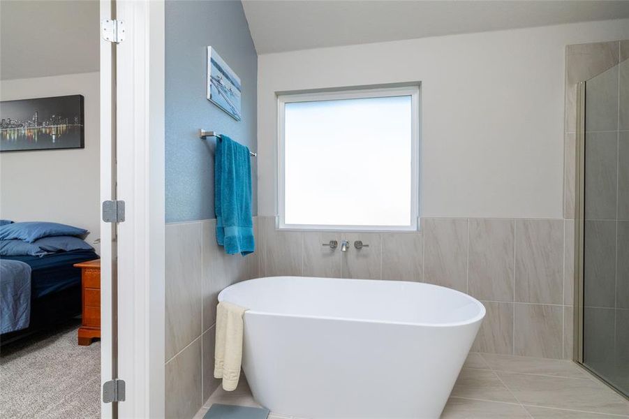 Ensuite bathroom with a freestanding tub, tile walls, a wainscoted wall, a shower with door, and light tile patterned floors