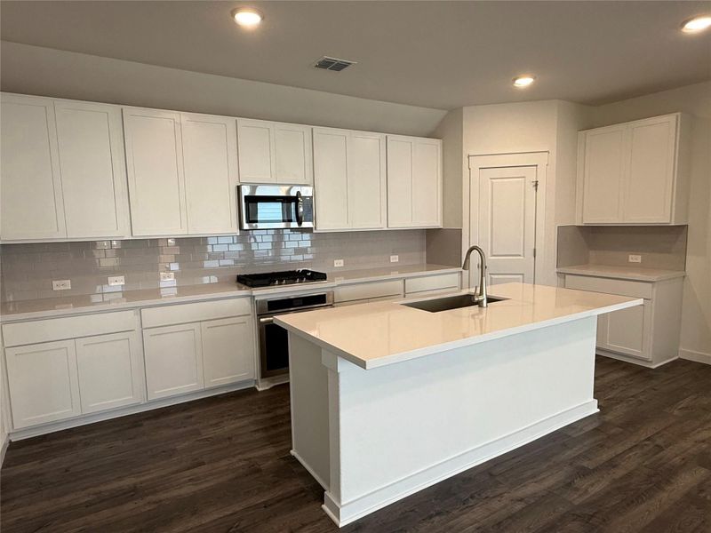 Kitchen featuring appliances with stainless steel finishes, dark wood-style flooring, tasteful backsplash, a center island with sink, and recessed lighting Kitchen featuring appliances with stainless steel finishes, dark wood-style flooring, tasteful backsplash, a center island with sink, and recessed lighting
