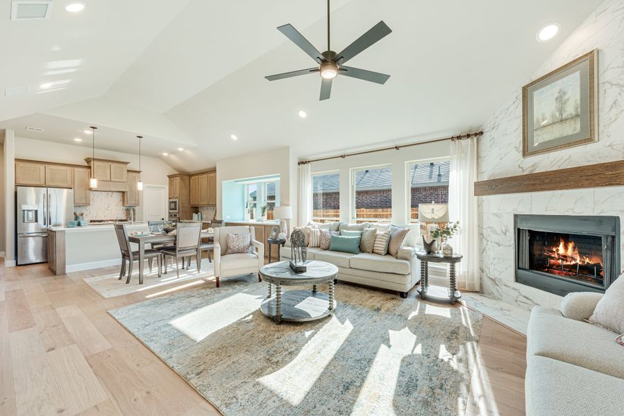 Open-concept living room with marble fireplace, vaulted ceiling, and hardwood floors open to kitchen and dining area.