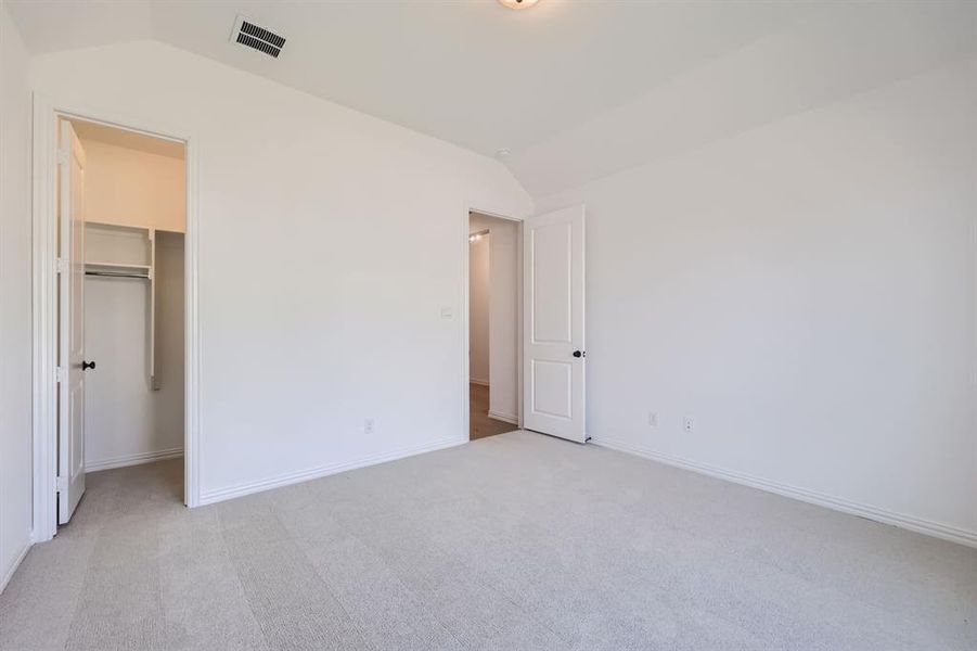 Unfurnished bedroom featuring a spacious closet, a closet, vaulted ceiling, and light colored carpet