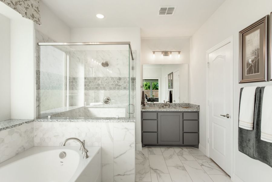 Master bathroom with marble soaking tub, glass-enclosed shower, and gray vanity with granite countertop