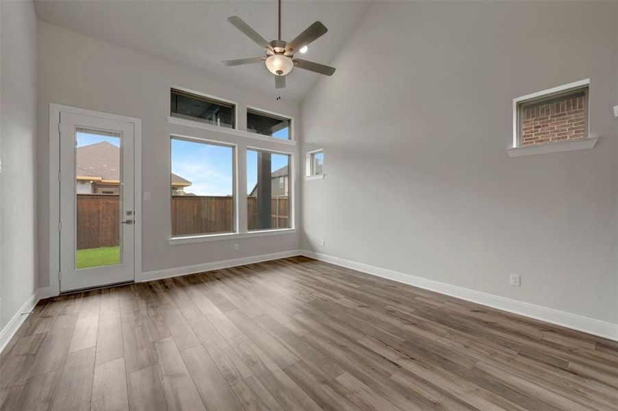 Spacious room featuring vaulted ceilings, wood-finish flooring, a ceiling fan with integrated lighting, and multiple windows including a full-light door providing exterior access