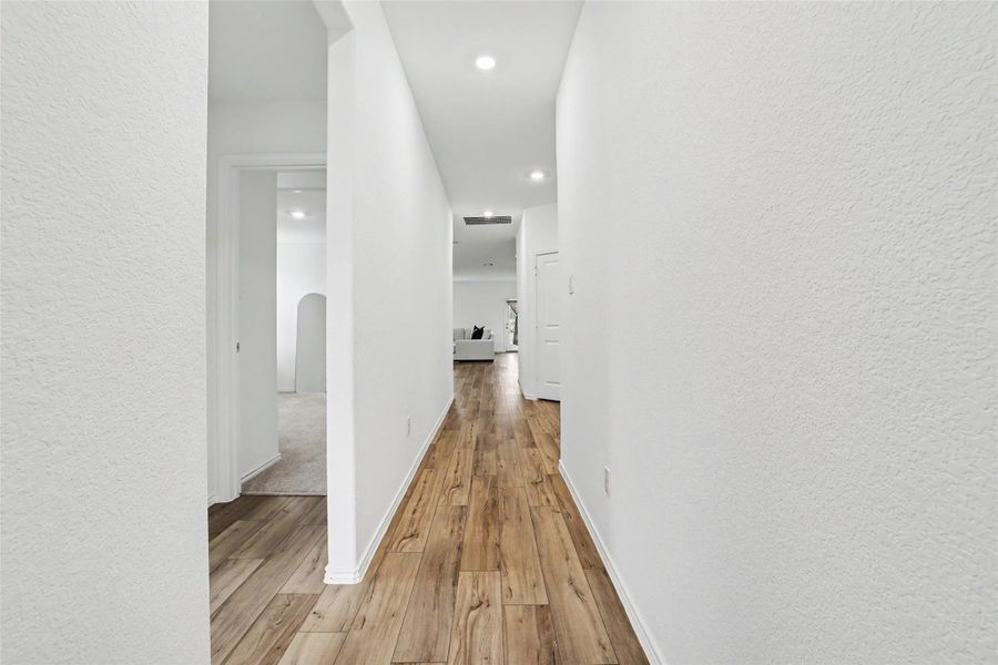 Long hallway featuring wood-finish flooring, white walls, and recessed lighting