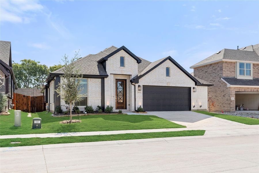 Single-story home with white brick exterior, dark two-car garage, and manicured front lawn Single-story home with white brick exterior, dark two-car garage, and manicured front lawn