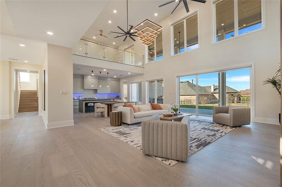 Living area with light wood-style floors, ceiling fan, recessed lighting, stairway, and a towering ceiling Living area with light wood-style floors, ceiling fan, recessed lighting, stairway, and a towering ceiling