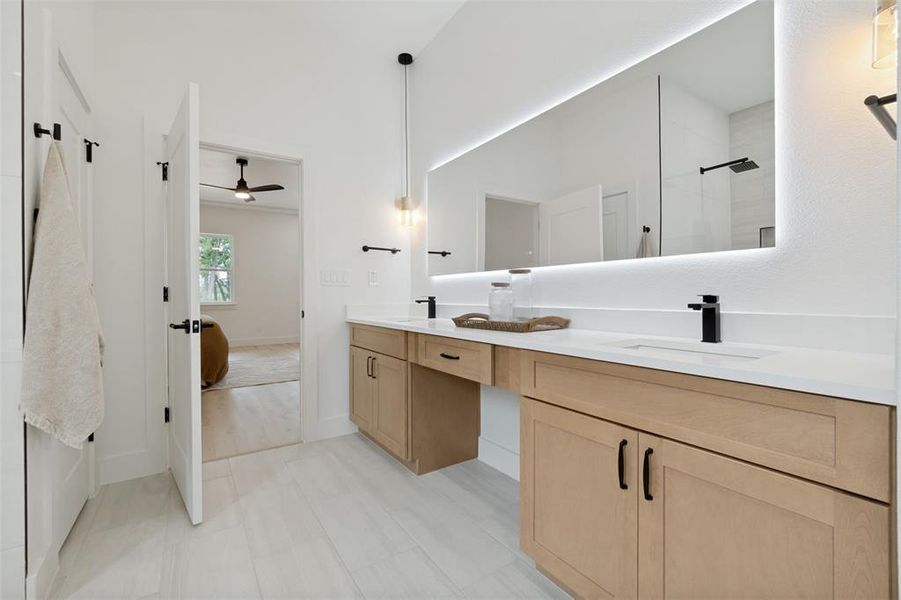 Contemporary bathroom featuring a double vanity with light wood cabinetry, white countertops, and matte black fixtures