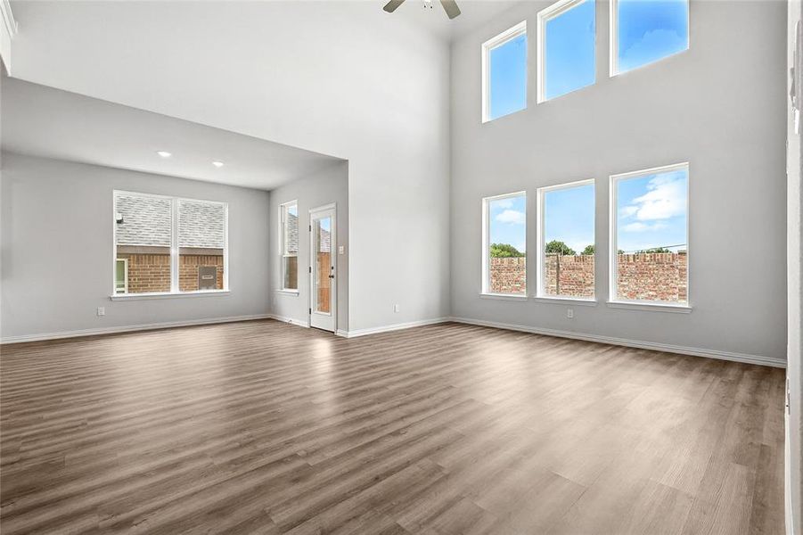 Unfurnished living room featuring ceiling fan, healthy amount of natural light, wood finished floors, and a towering ceiling Unfurnished living room featuring ceiling fan, healthy amount of natural light, wood finished floors, and a towering ceiling