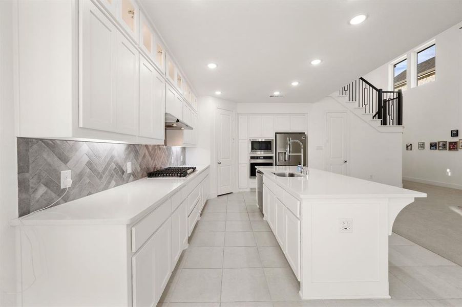 Kitchen with white cabinets, a kitchen island with sink, light stone countertops, recessed lighting, and glass insert cabinets