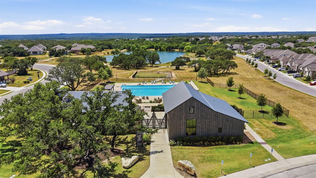 An aerial panorama reveals a picturesque community featuring a sparkling pool, modern clubhouse, and serene lake, all bordered by verdant landscapes and residential streets.