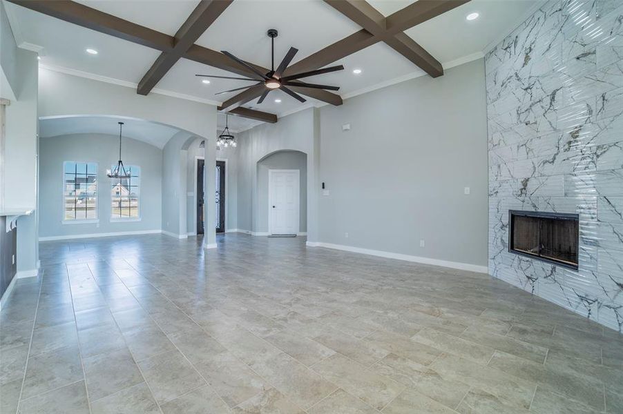 Unfurnished living room with a fireplace, coffered ceiling, a chandelier, arched walkways, and beamed ceiling Unfurnished living room with a fireplace, coffered ceiling, a chandelier, arched walkways, and beamed ceiling