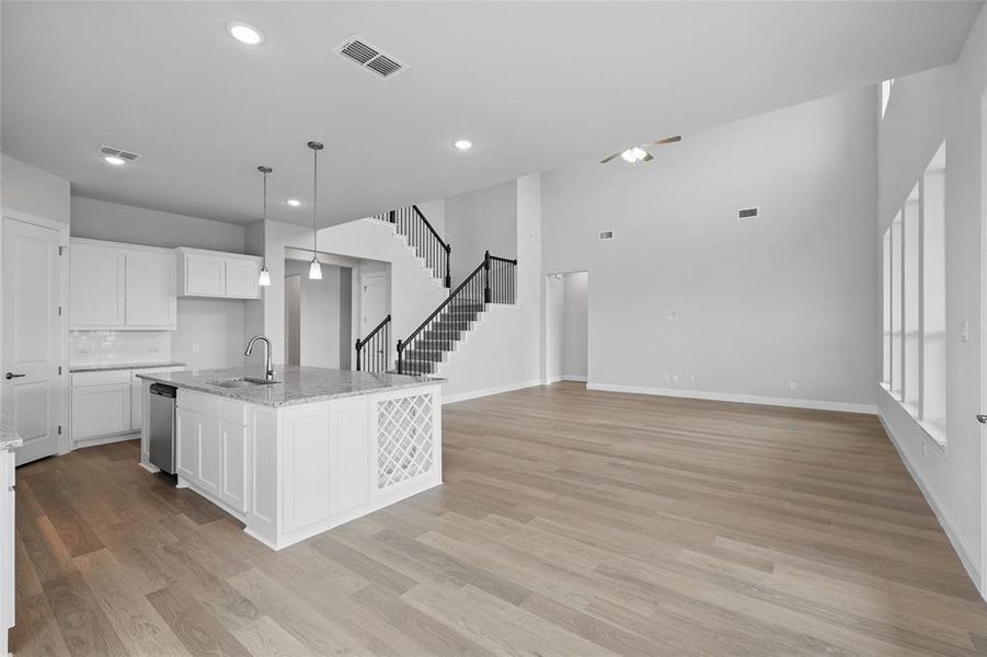 Kitchen with stainless steel dishwasher, a sink, light wood finished floors, white cabinetry, and recessed lighting