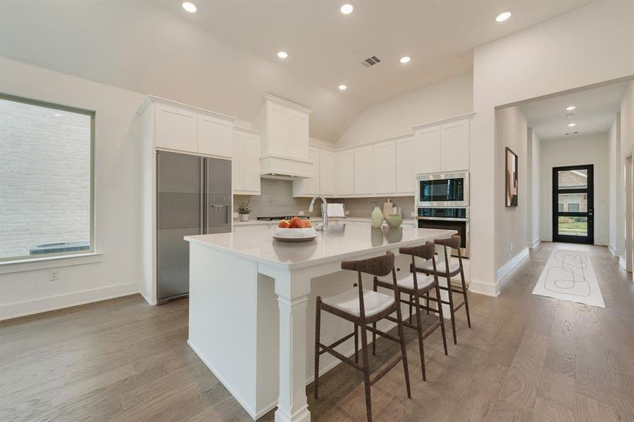 Kitchen with white cabinets, decorative backsplash, a kitchen breakfast bar, light wood-type flooring, and recessed lighting
