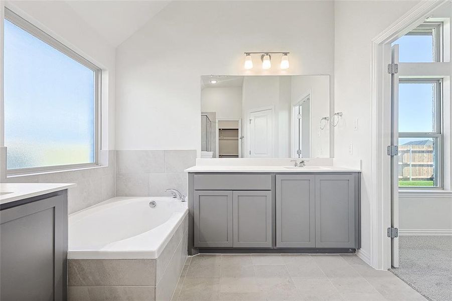 Bathroom featuring vanity, tiled bath, vaulted ceiling, and a wealth of natural light