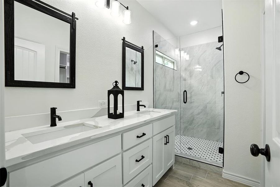Bathroom with a marble finish shower, double vanity, and wood finish floors