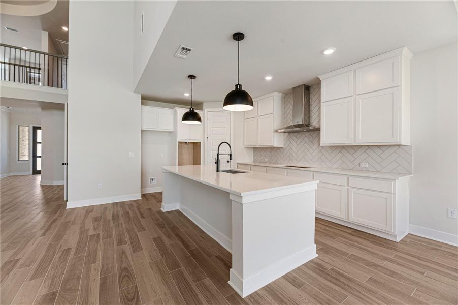 Kitchen featuring tasteful backsplash, a kitchen island with sink, a kitchen bar, wall chimney range hood, and pendant lighting