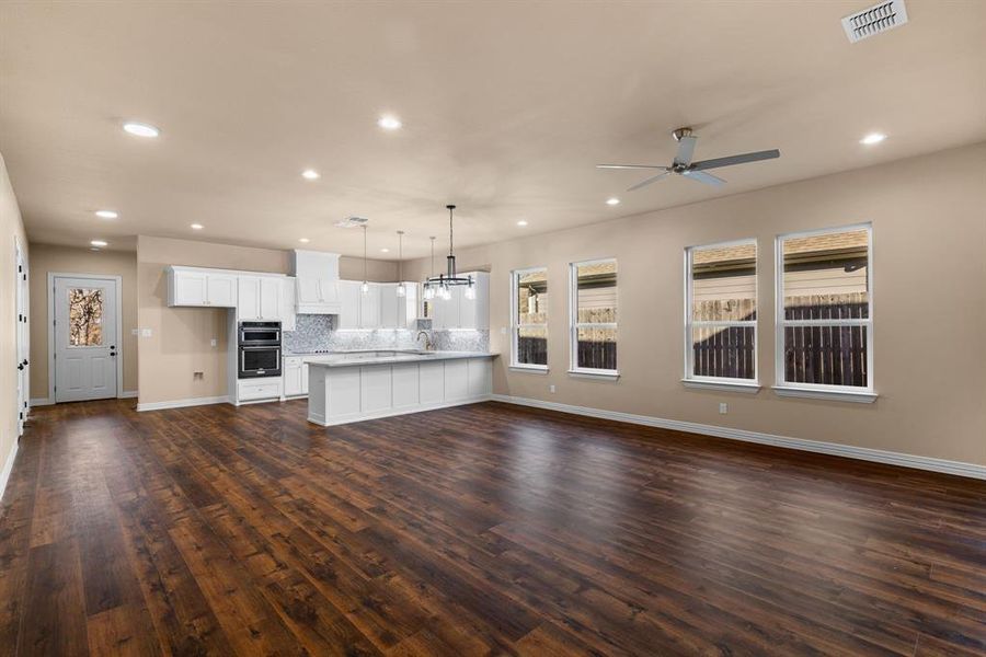 Unfurnished living room featuring dark hardwood / wood-style flooring, sink, and ceiling fan with notable chandelier