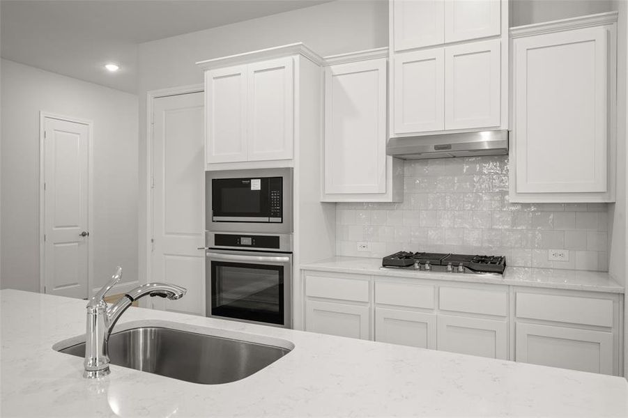 Kitchen featuring stainless steel appliances, under cabinet range hood, white cabinetry, tasteful backsplash, and recessed lighting