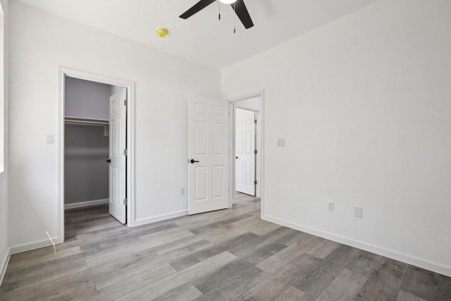 Bedroom 3 with a walk in closet, light wood-type laminate flooring, and a ceiling fan