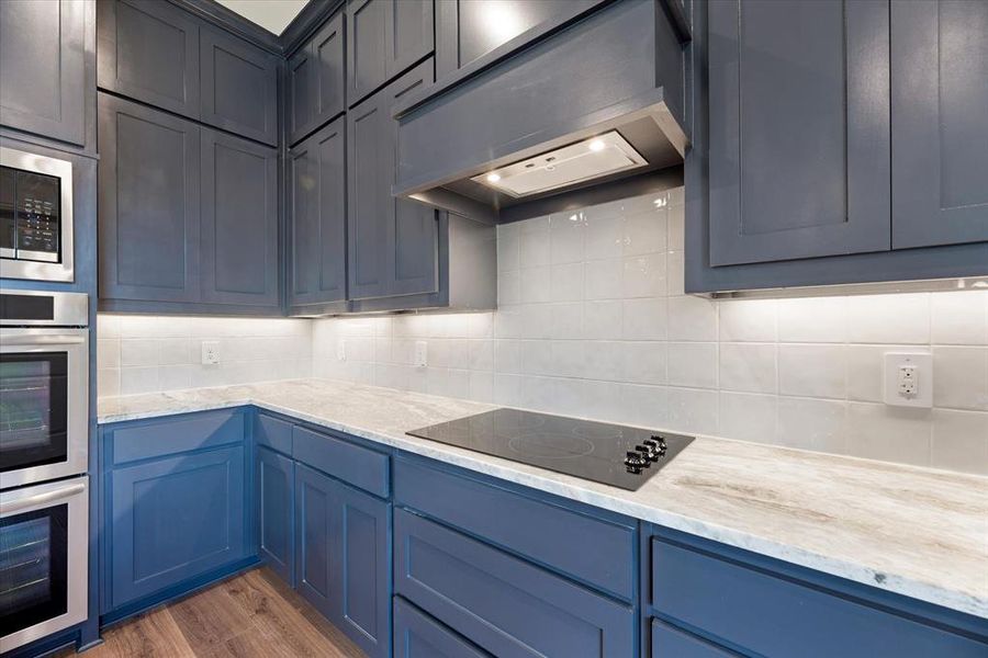 Kitchen featuring light stone countertops, dark wood-type flooring, double oven, black electric stovetop, and tasteful backsplash